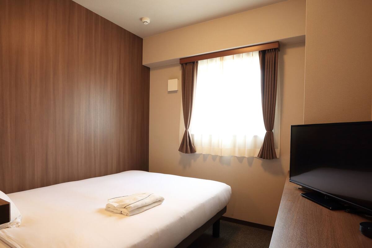 Une chambre d’hôtel avec un lit, une télévision et une fenêtre avec des rideaux.