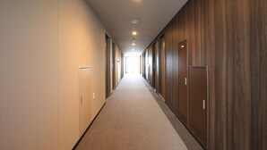 A long, narrow hallway with a carpeted floor, wooden panel walls, and doors on both sides. - Smile Hotel Hakata Ekimae (Fukuoka)