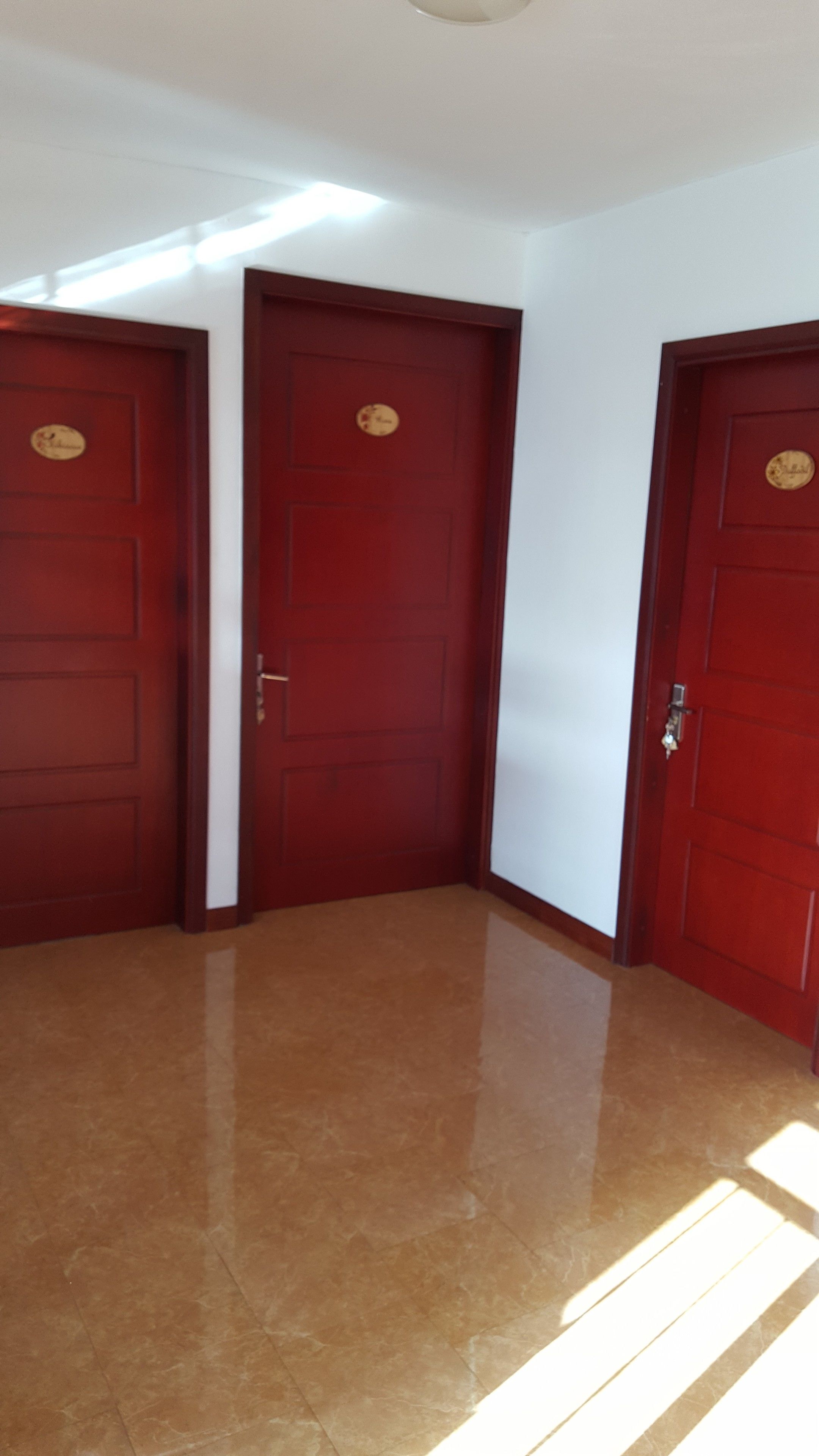 A hallway with three wooden doors, each with a nameplate, leading to rooms. The floor is shiny, and the walls are white.