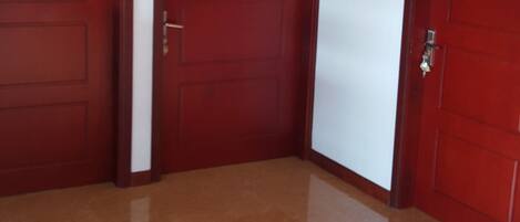 A hallway with three wooden doors, each with a nameplate, leading to rooms. The floor is shiny, and the walls are white.