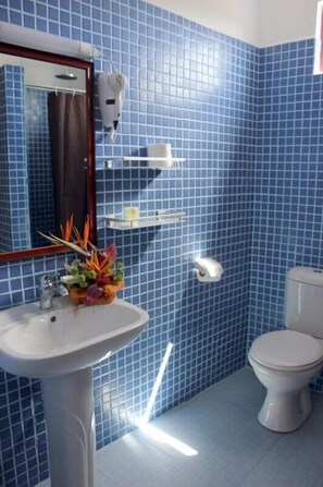 Un baño con paredes de azulejos azules, un lavamanos blanco, un inodoro y un espejo.