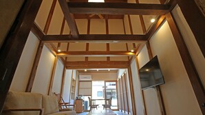 Un interior japonés tradicional con suelo de tatami, vigas de madera, un televisor y una puerta corrediza que da a otra habitación.