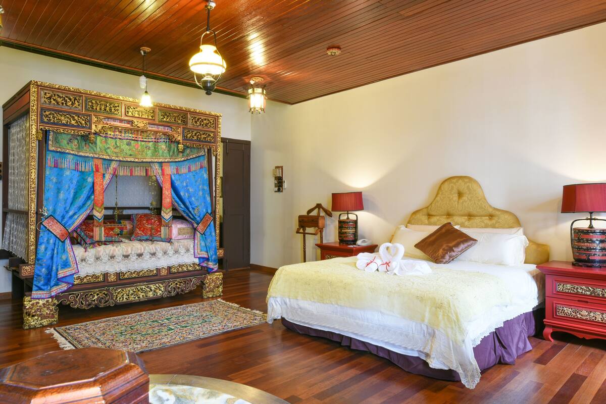 A traditional room with a four-poster bed, a red nightstand, and a wooden ceiling.