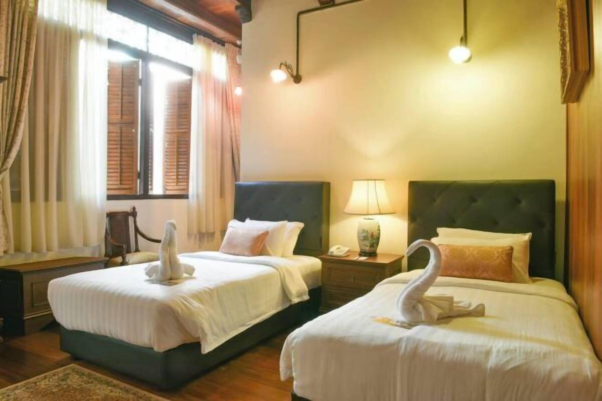 A hotel room with two beds, each with a swan-shaped towel, a bedside lamp, and a wooden headboard.