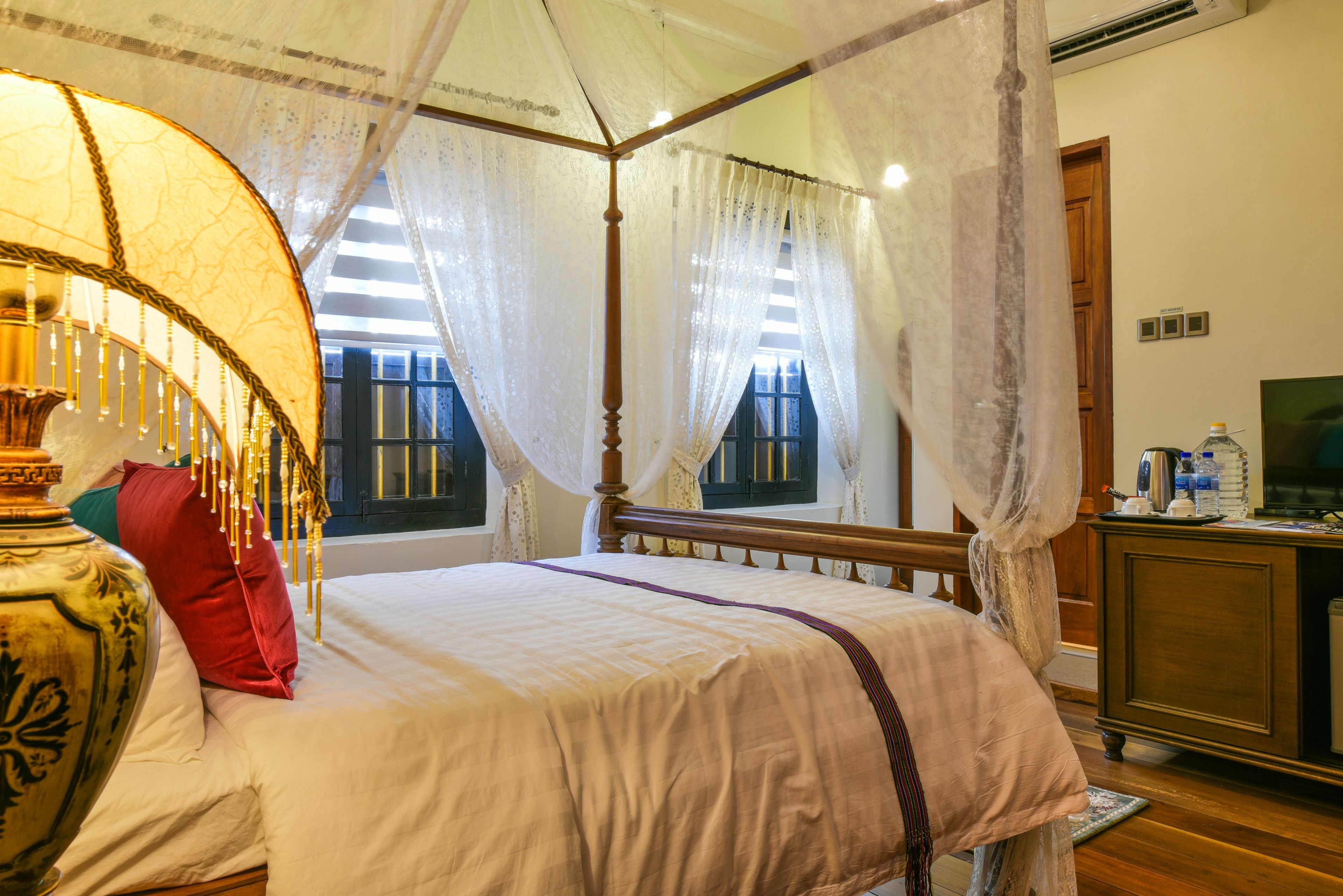 A four-poster bed with a canopy, a large vase, and a red pillow.