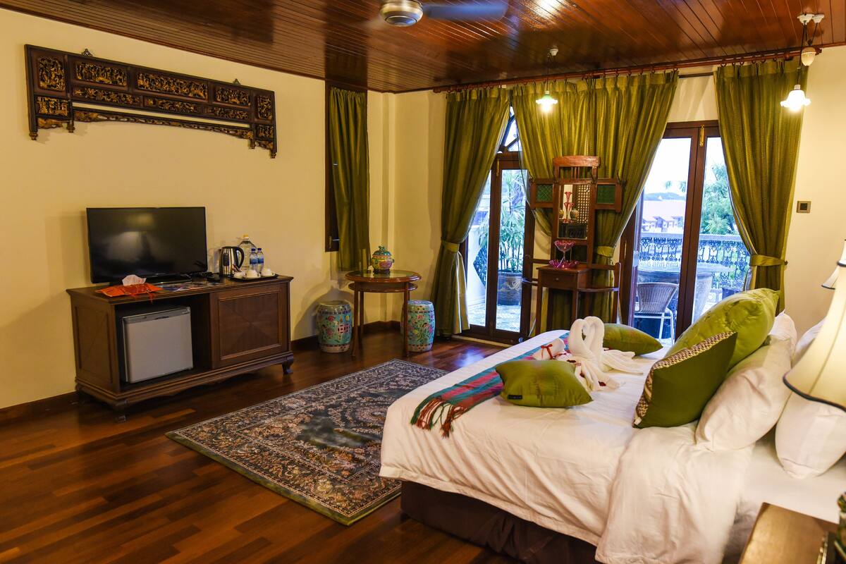 A well-furnished hotel room with a bed, a television, a small refrigerator, a coffee maker, a decorative vase, and a view of the outside balcony.