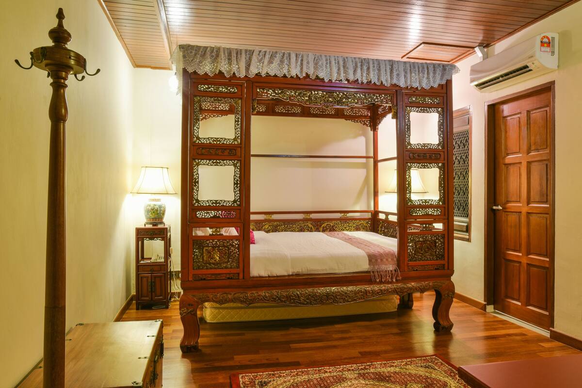 A traditional four-poster bed with intricate woodwork, a bedside table with a lamp, and a wooden floor.