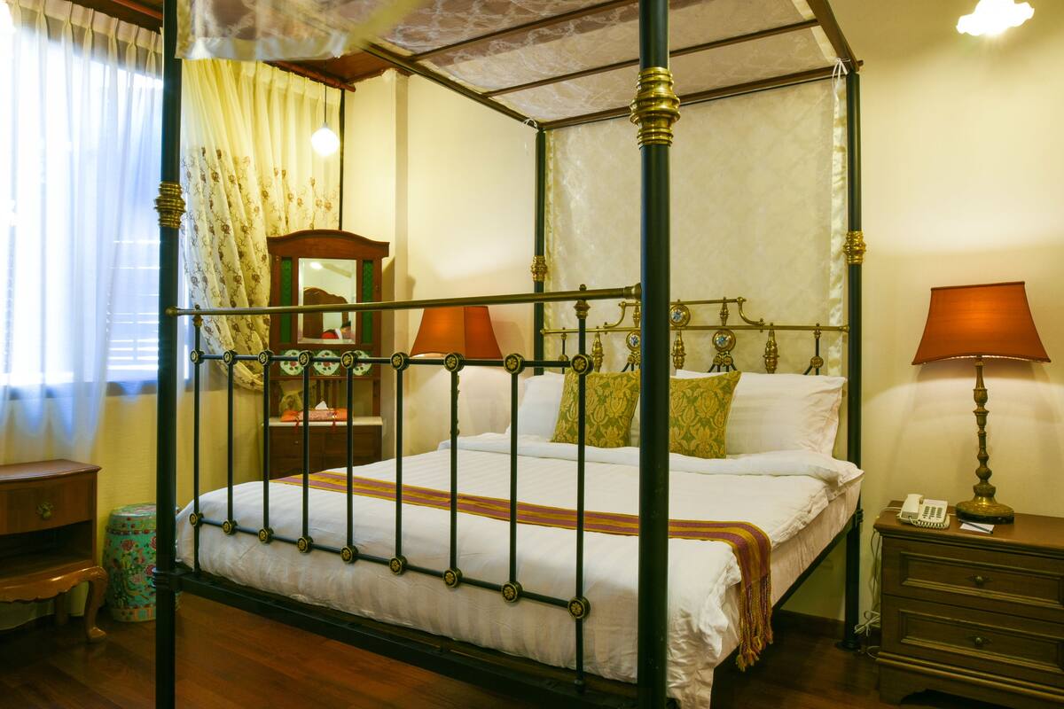 A four-poster canopy bed with a wooden frame and brass accents, a bedside table with a lamp, and a mirror above the bed.