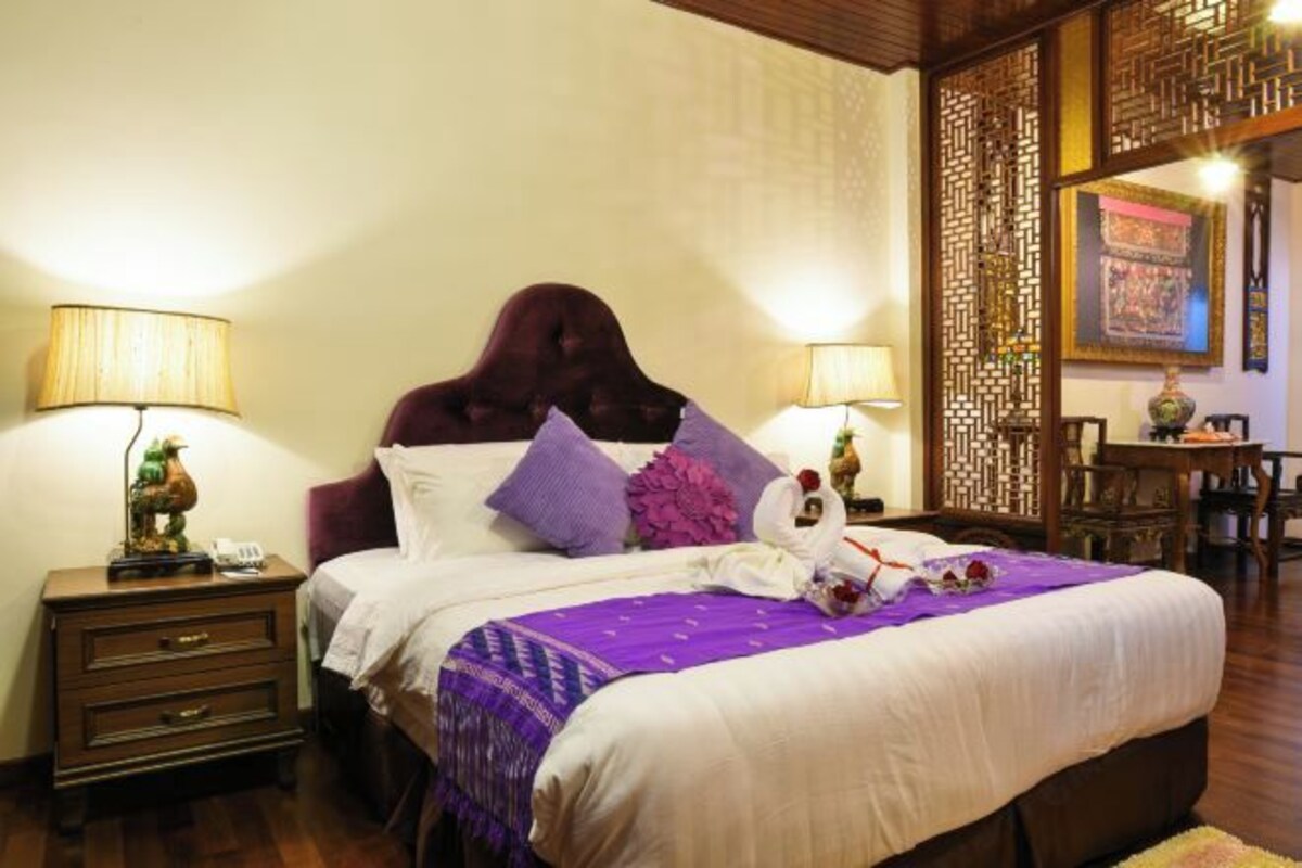 A hotel room with a large bed, two bedside tables with lamps, a wooden headboard, and a decorative screen.