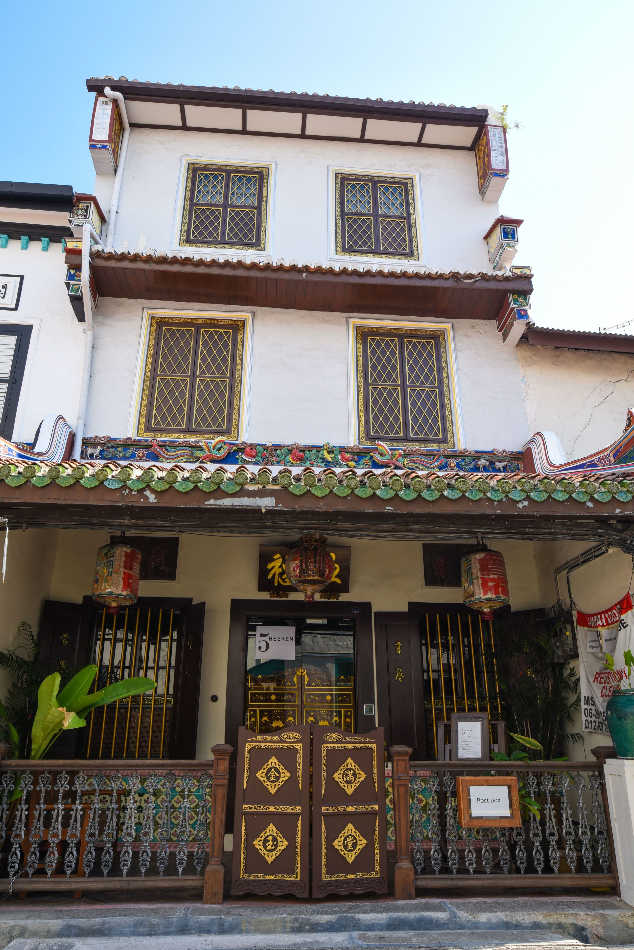 Un bâtiment traditionnel avec un toit en tuiles, un portail d’entrée avec une enseigne et une petite boîte aux lettres.