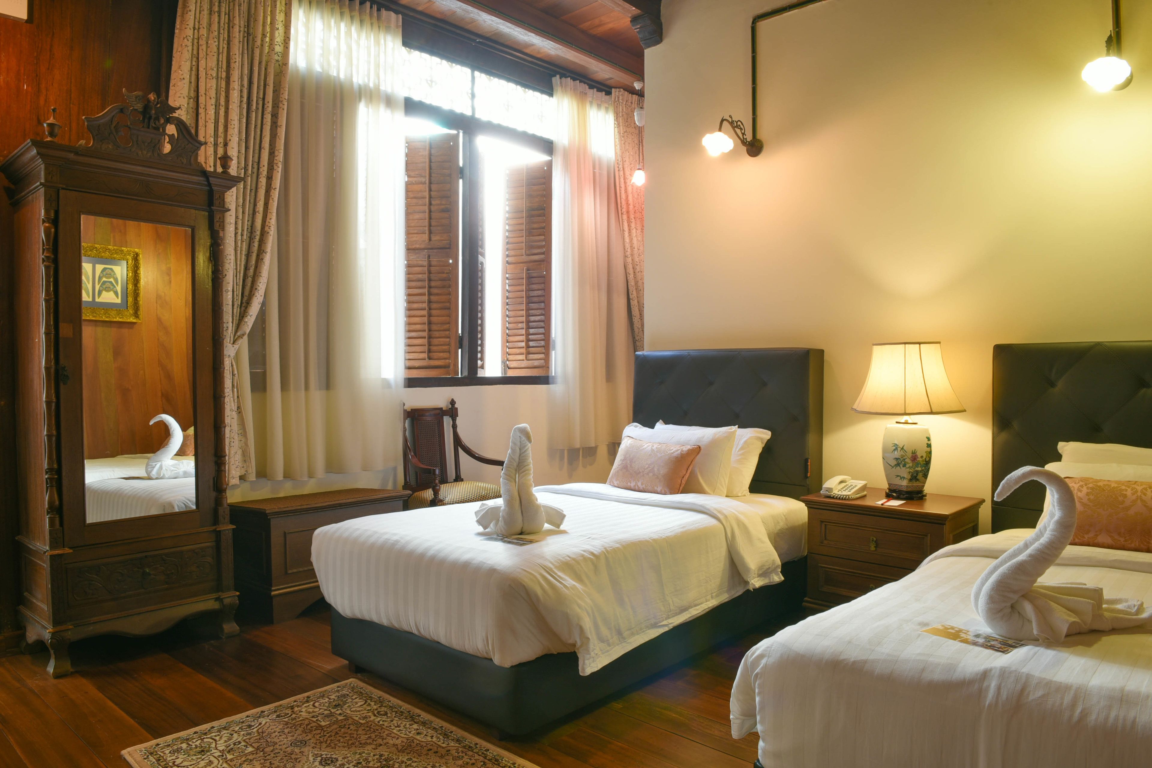 A hotel room with two beds, a wooden dresser, a mirror, a nightstand with a lamp, and a window with curtains.