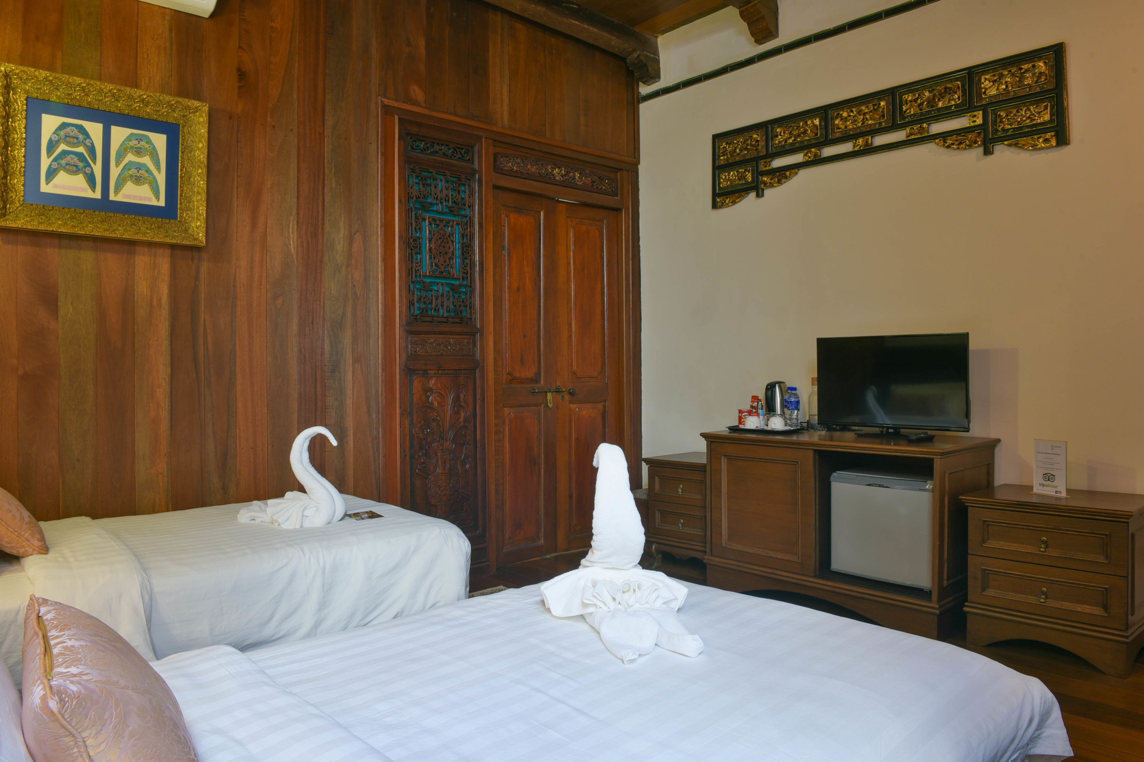 A hotel room with two beds, a television, a minibar, and a wooden wardrobe.