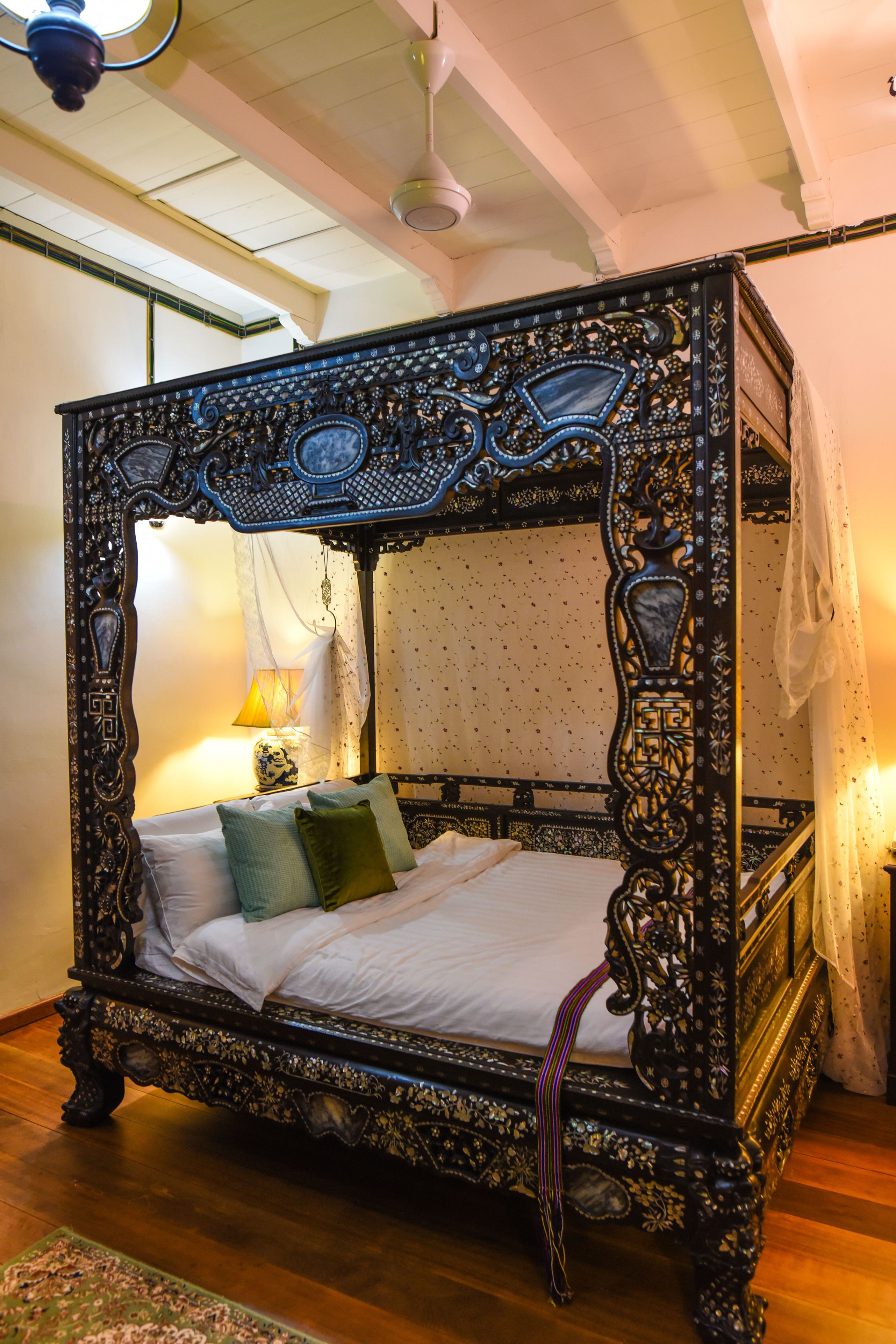 A four-poster bed with intricate carvings, a canopy, and a nightstand with a lamp.