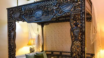 A four-poster bed with intricate carvings, a canopy, and a nightstand with a lamp.