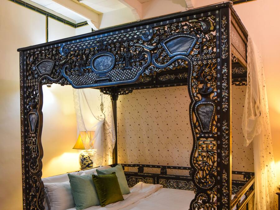 A four-poster bed with intricate carvings, a canopy, and a nightstand with a lamp.