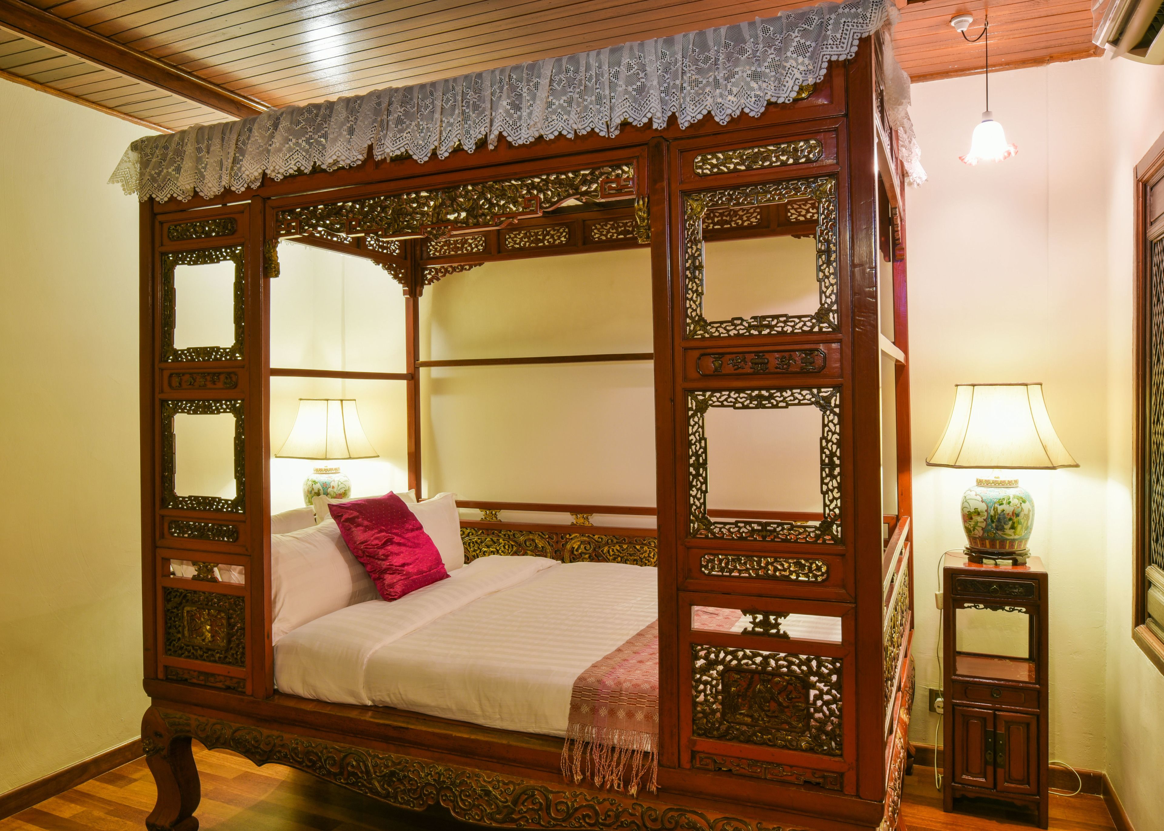Una cama con dosel adornada con detalles de madera labrada y un dosel de encaje.