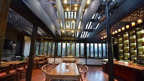A restaurant with wooden tables and chairs, a bar area, and large windows allowing natural light.
