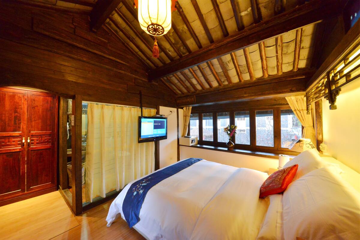 Puinen huone, jossa on sänky, televisio ja ikkuna, jossa on verhot.