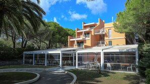 A modern building with a glass-enclosed patio area, surrounded by trees and a well-maintained lawn. - TH Lacona (Capoliveri)