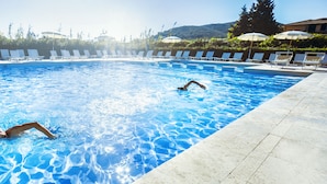 A swimming pool with two people swimming, surrounded by lounge chairs and umbrellas. - TH Lacona (Capoliveri)