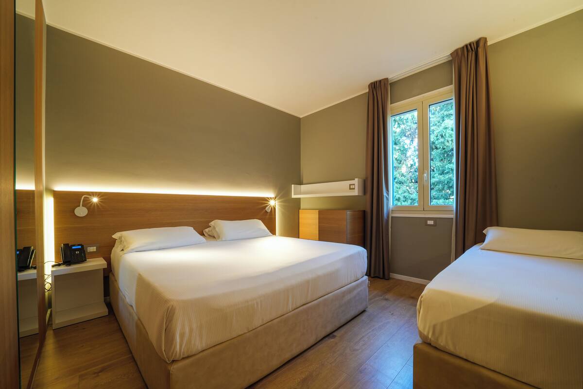 A hotel room with two beds, a bedside table with a phone, and a window with curtains.