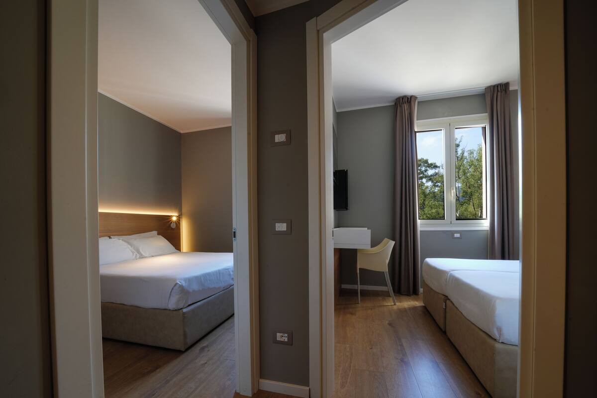 A hotel room with two beds, a desk, a chair, and a window with curtains.