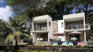 A modern hotel with a pool, outdoor seating, and a stone facade. - Valmarin Seafront Apartments (Trou d'Eau Douce)