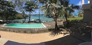 A swimming pool surrounded by palm trees and a view of the sea. - Valmarin Seafront Apartments (Trou d'Eau Douce)