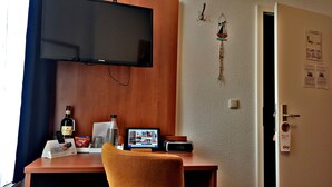 Een hotelkamer met een houten bureau, een televisie, een klok en een deur met een bordje.