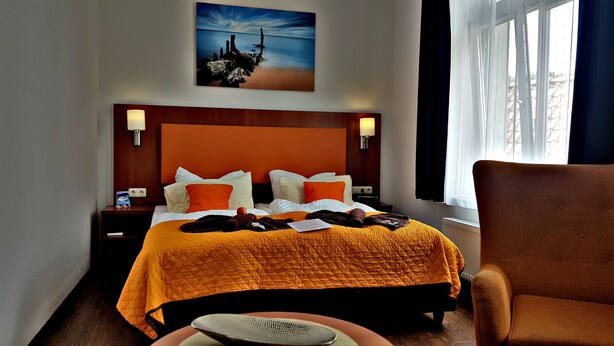 Een hotelkamer met een groot bed, een stoel, een nachtkastje en een schilderij aan de muur.