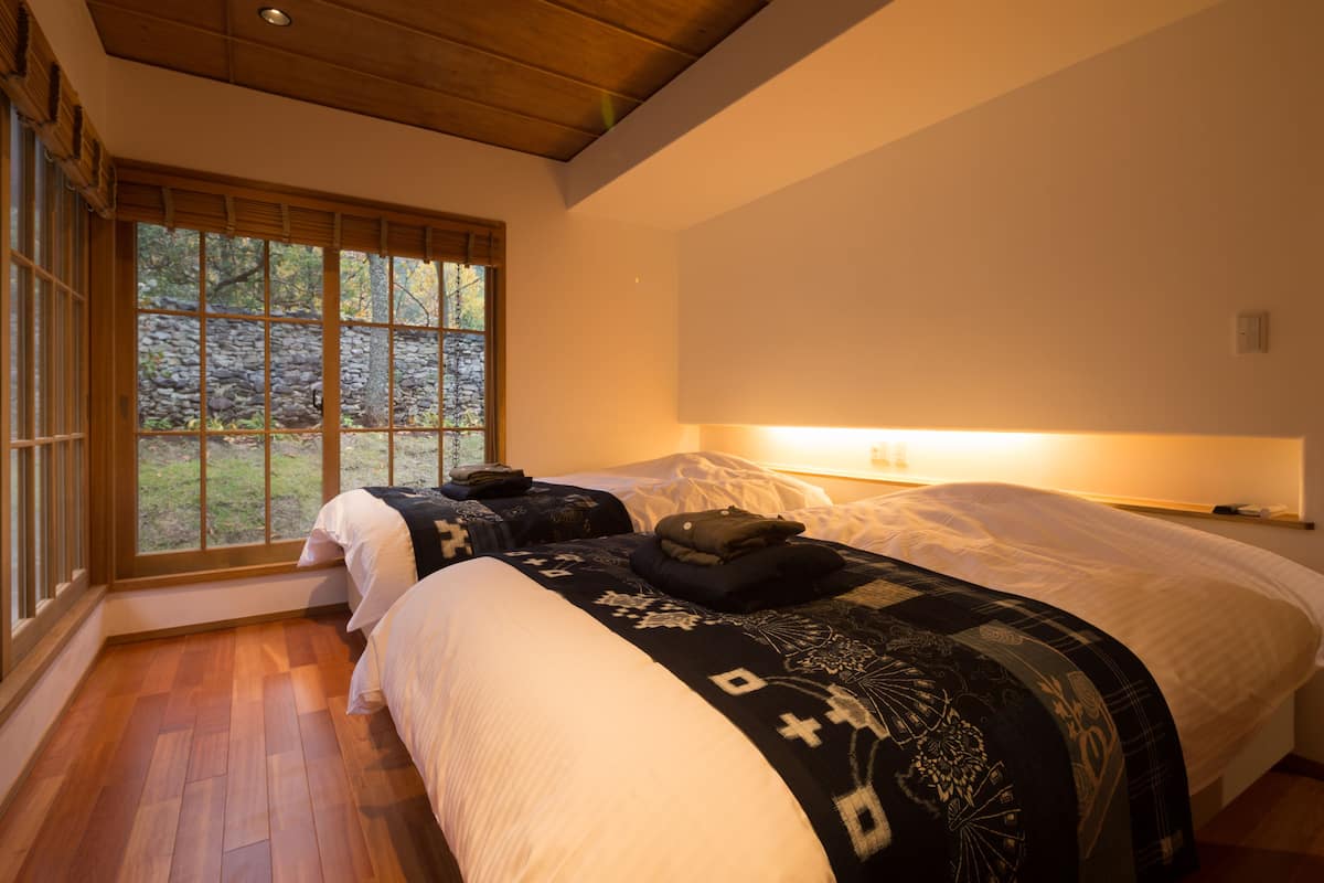 Un dormitorio con dos camas, un ventanal grande y techo de madera.