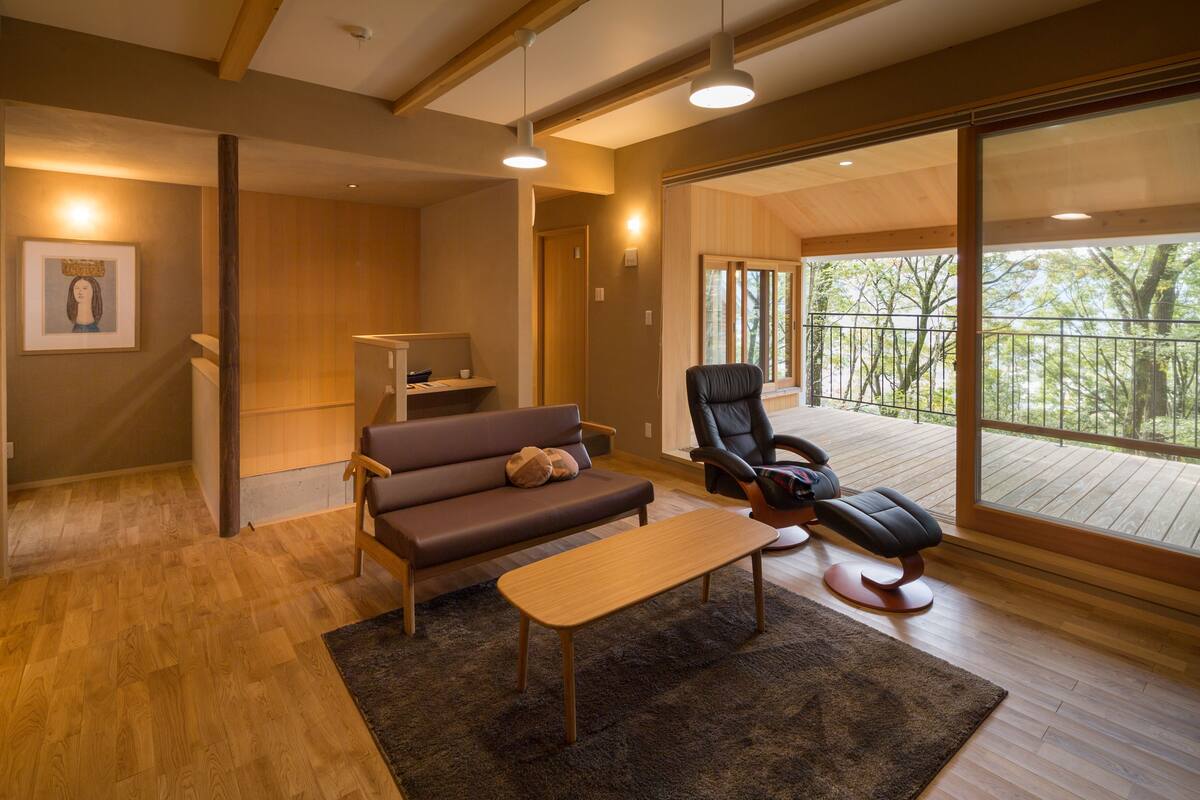Una sala de estar moderna con suelo de madera, un sofá marrón, un sillón de cuero negro y una mesa de centro de madera.