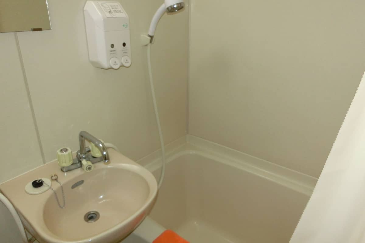 Un baño con lavamanos, grifo y cabezal de ducha manual fijado a la pared.