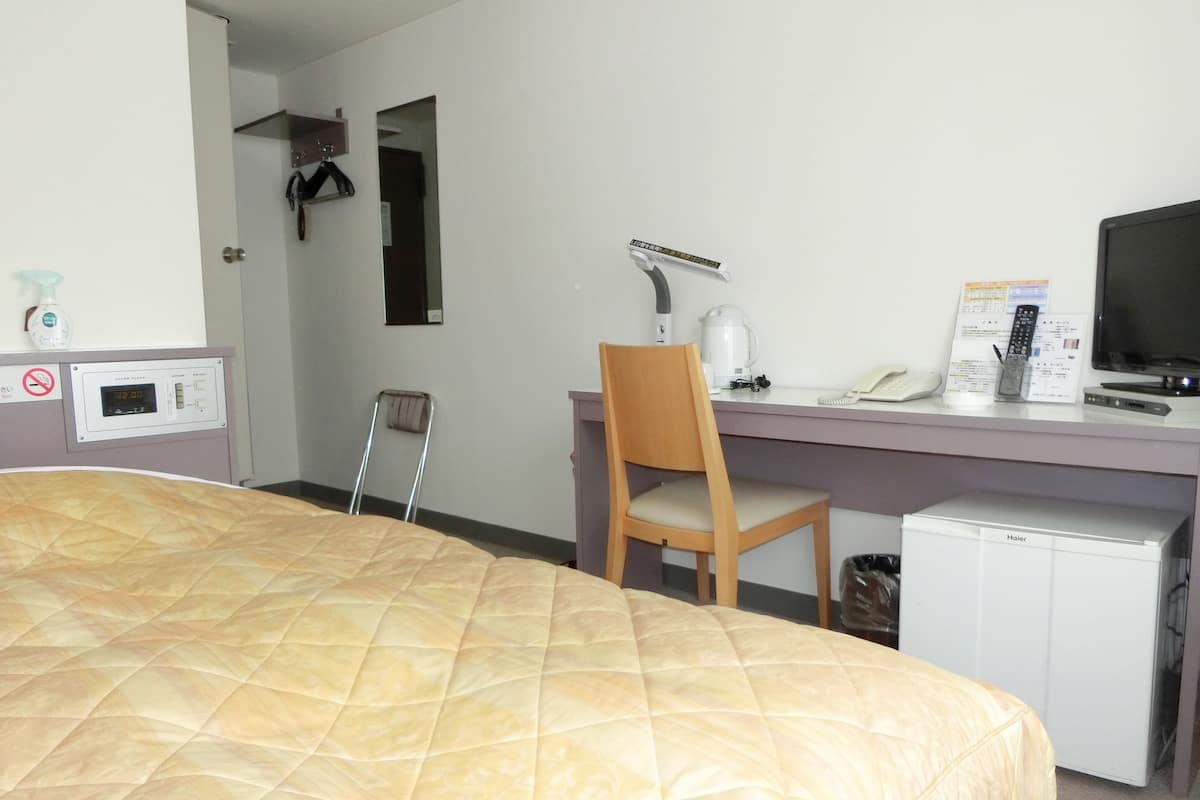 Habitación de hotel con cama, escritorio con silla, refrigerador pequeño, televisor y reloj.