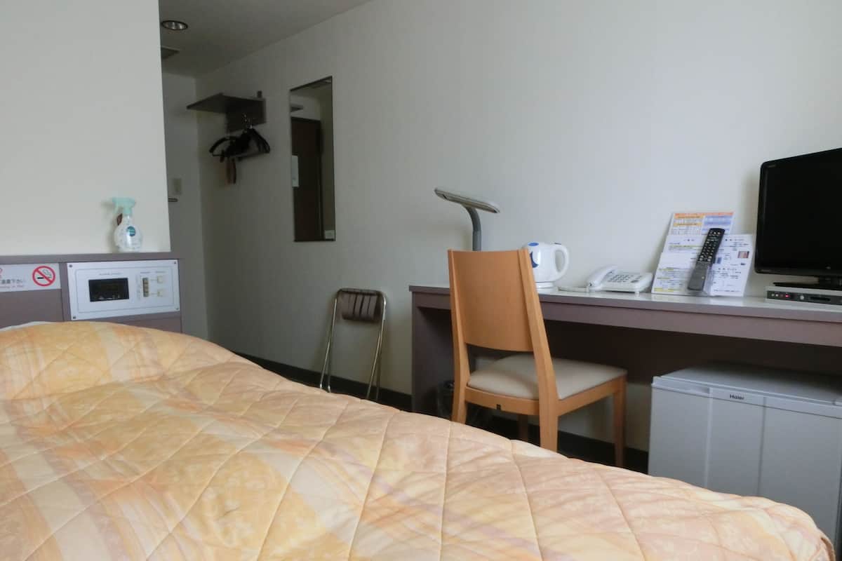 Una habitación de hotel con cama, escritorio con silla, televisor, microondas y refrigerador pequeño.