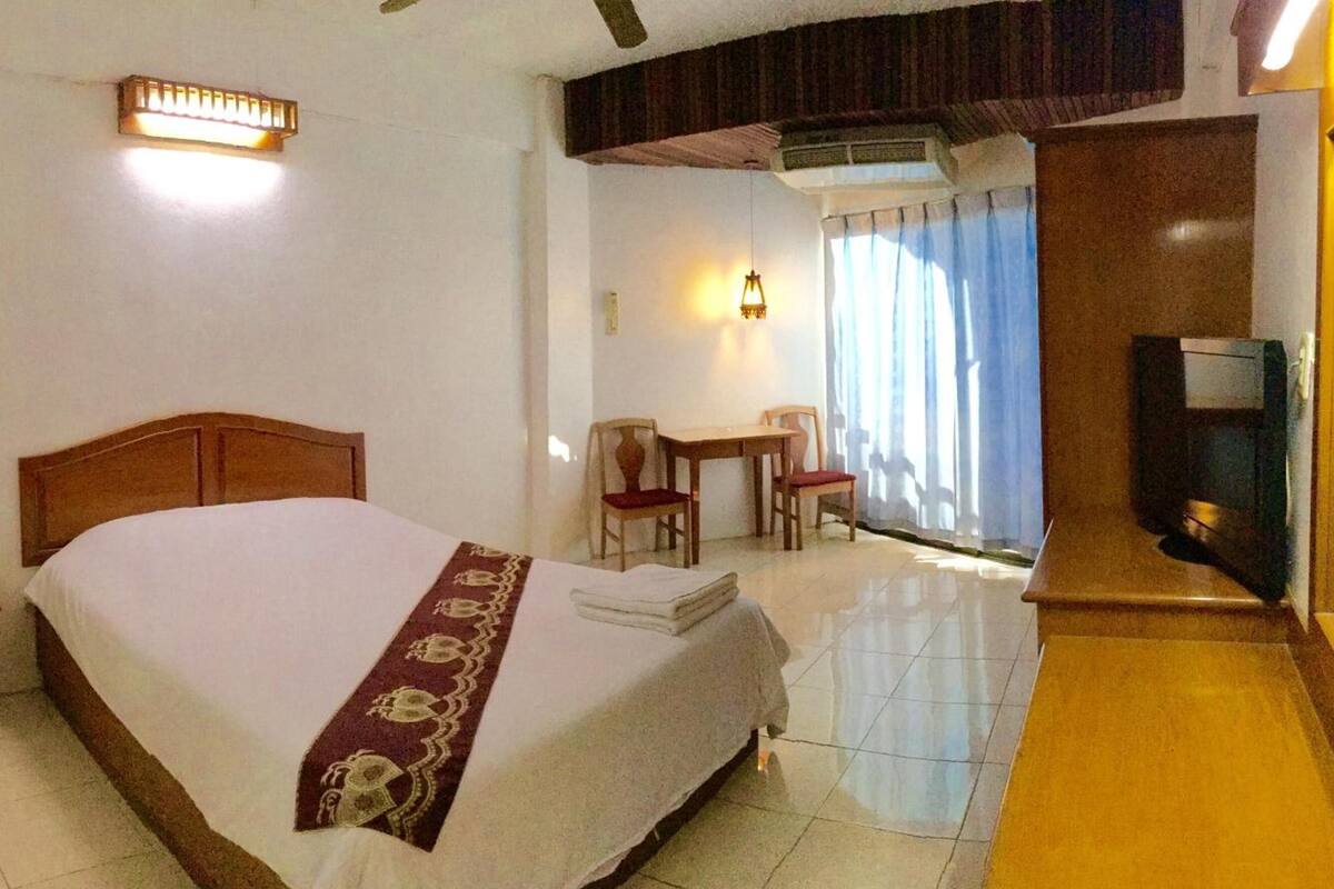A hotel room with a large bed, a desk with two chairs, a television, and a window with curtains.