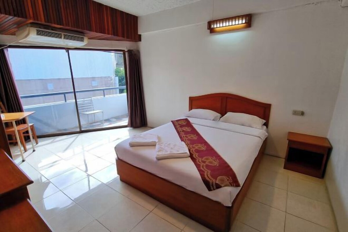 Een hotelkamer met een groot bed, een klein bureau, een stoel, een nachtkastje en een glazen schuifdeur naar een buitenruimte.