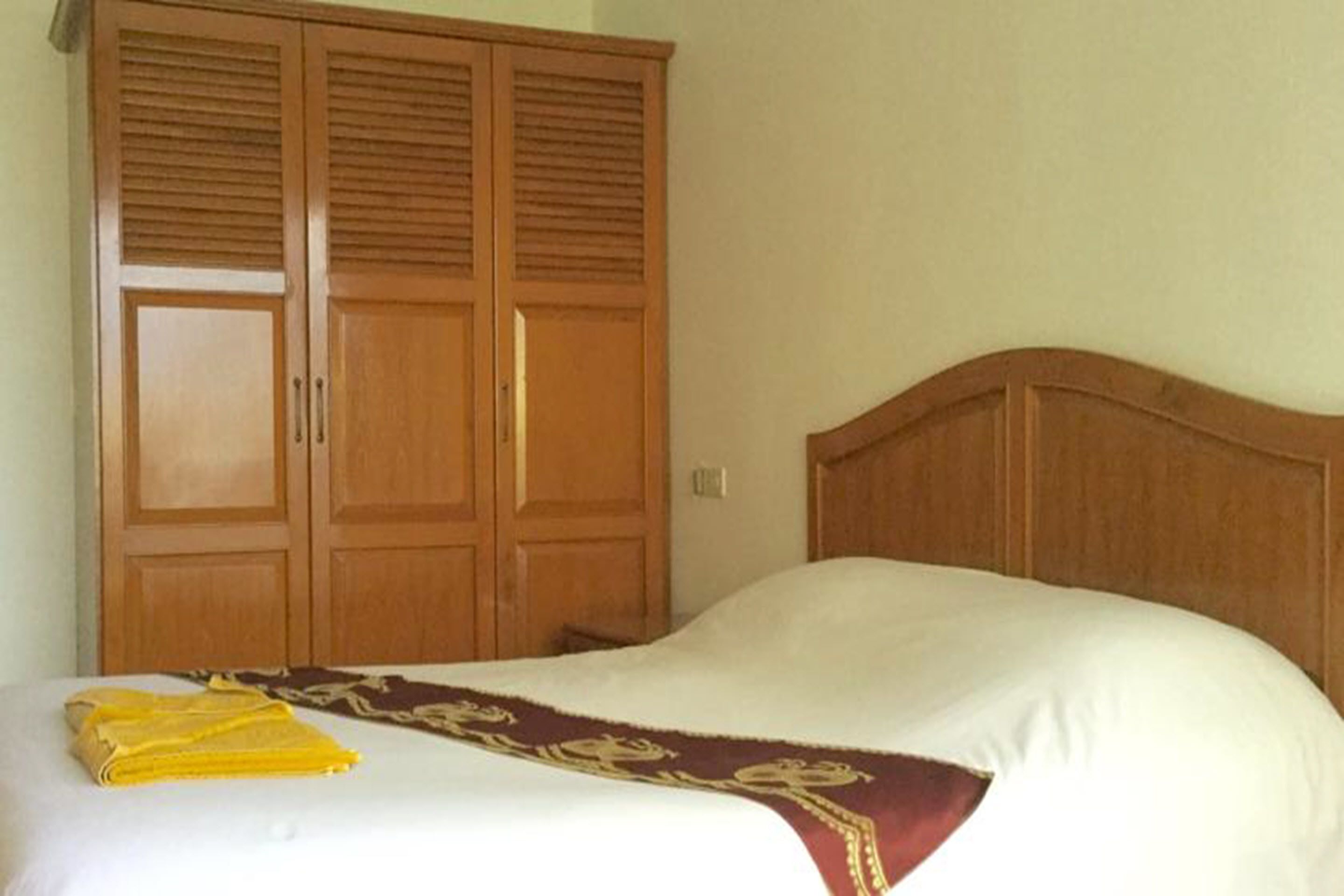 A bedroom with a bed, a wooden wardrobe, and a bedspread.