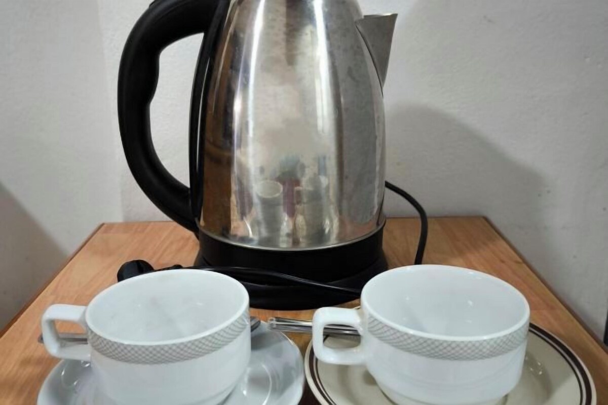Una tetera de acero inoxidable sobre una mesa con dos tazas y platillos blancos.