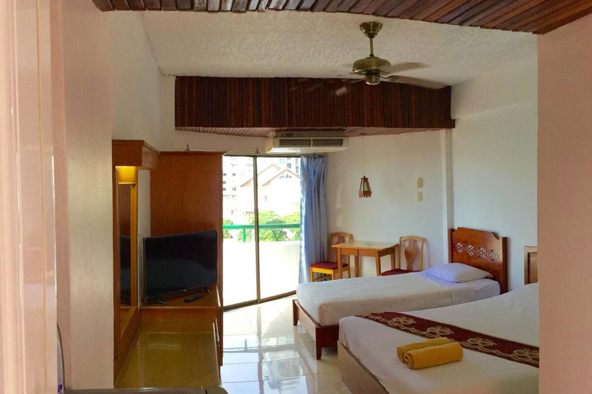 A hotel room with two beds, a television, a ceiling fan, and a view of the outside.