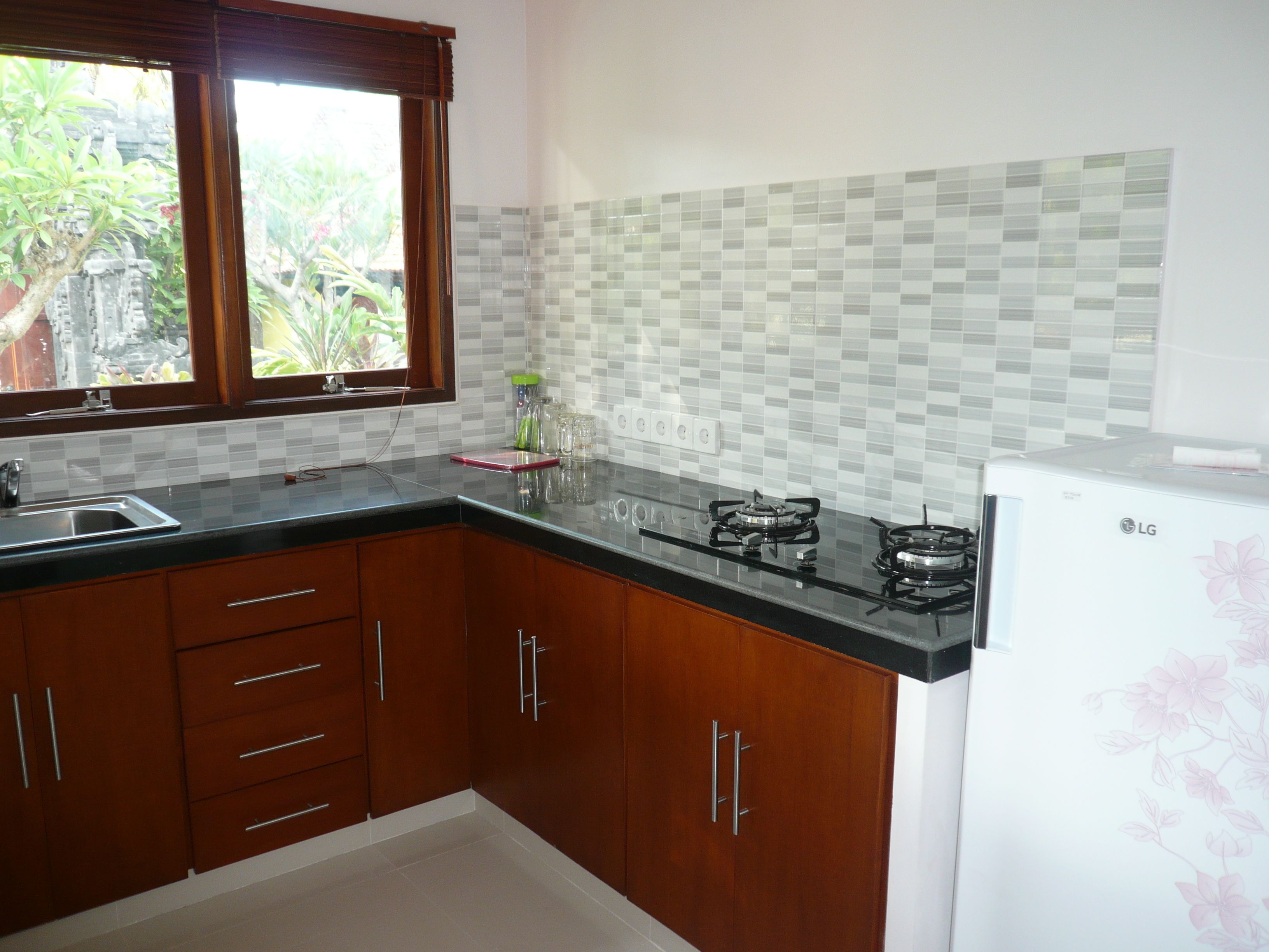 Una cocina con armarios de madera, encimera negra, ventana con vistas a zonas verdes y un refrigerador LG.