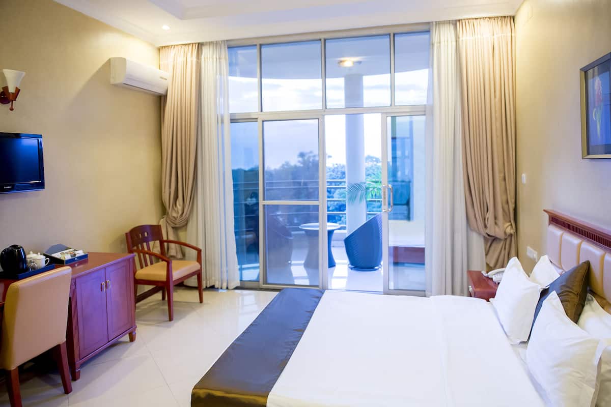A hotel room with a large bed, a desk with a chair, a television, and a balcony with a table and chairs.