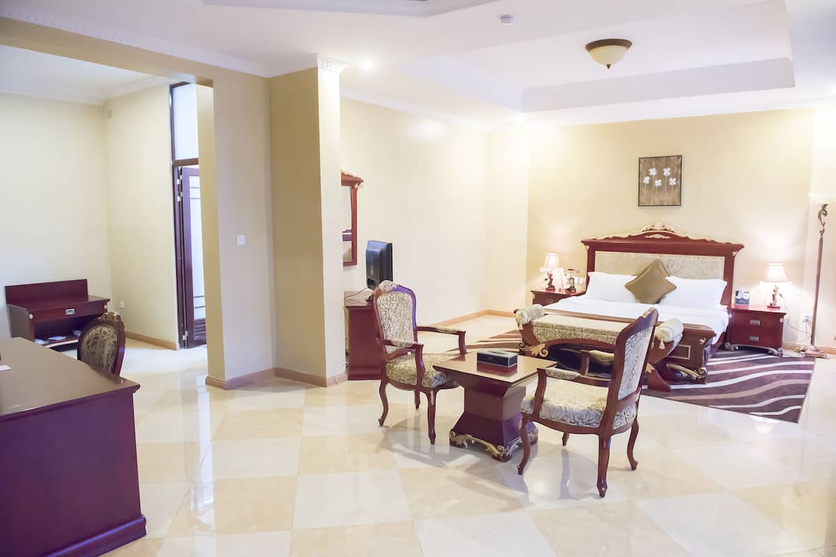 A hotel room with a bed, a desk, two chairs, a nightstand, and a lamp.