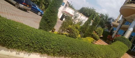 A landscaped area with a curved hedge, a paved walkway, and a building with a balcony.