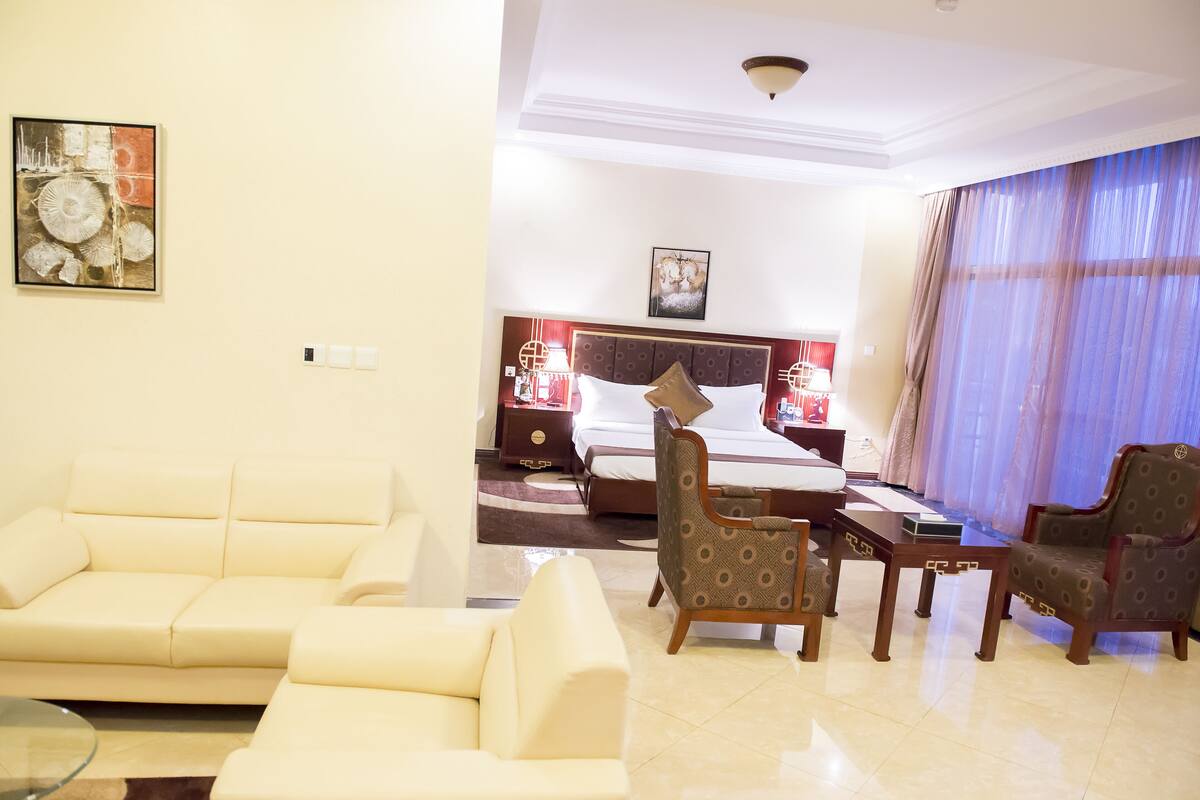A hotel room with a bed, a sofa, two armchairs, a small table, and a painting on the wall.