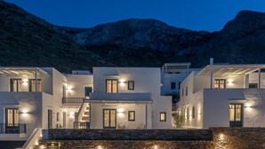 A modern, multi-story building with white walls and multiple balconies, set against a mountainous backdrop. - Sifnos House - Rooms & Spa (Sifnos)