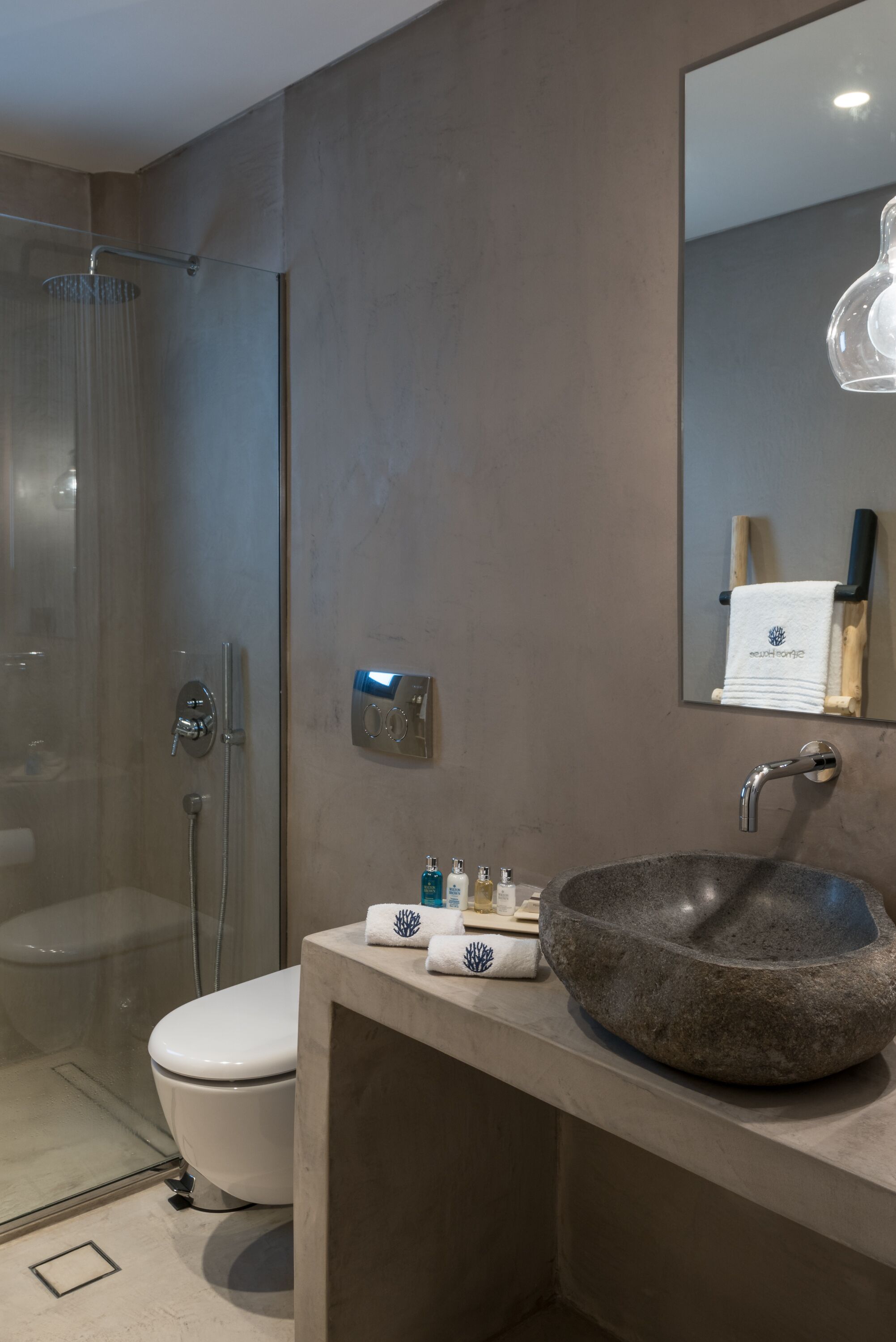 A modern bathroom with a glass-enclosed shower, a white toilet, and a large stone sink with a mirror above.