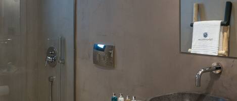 A modern bathroom with a glass-enclosed shower, a white toilet, and a large stone sink with a mirror above.