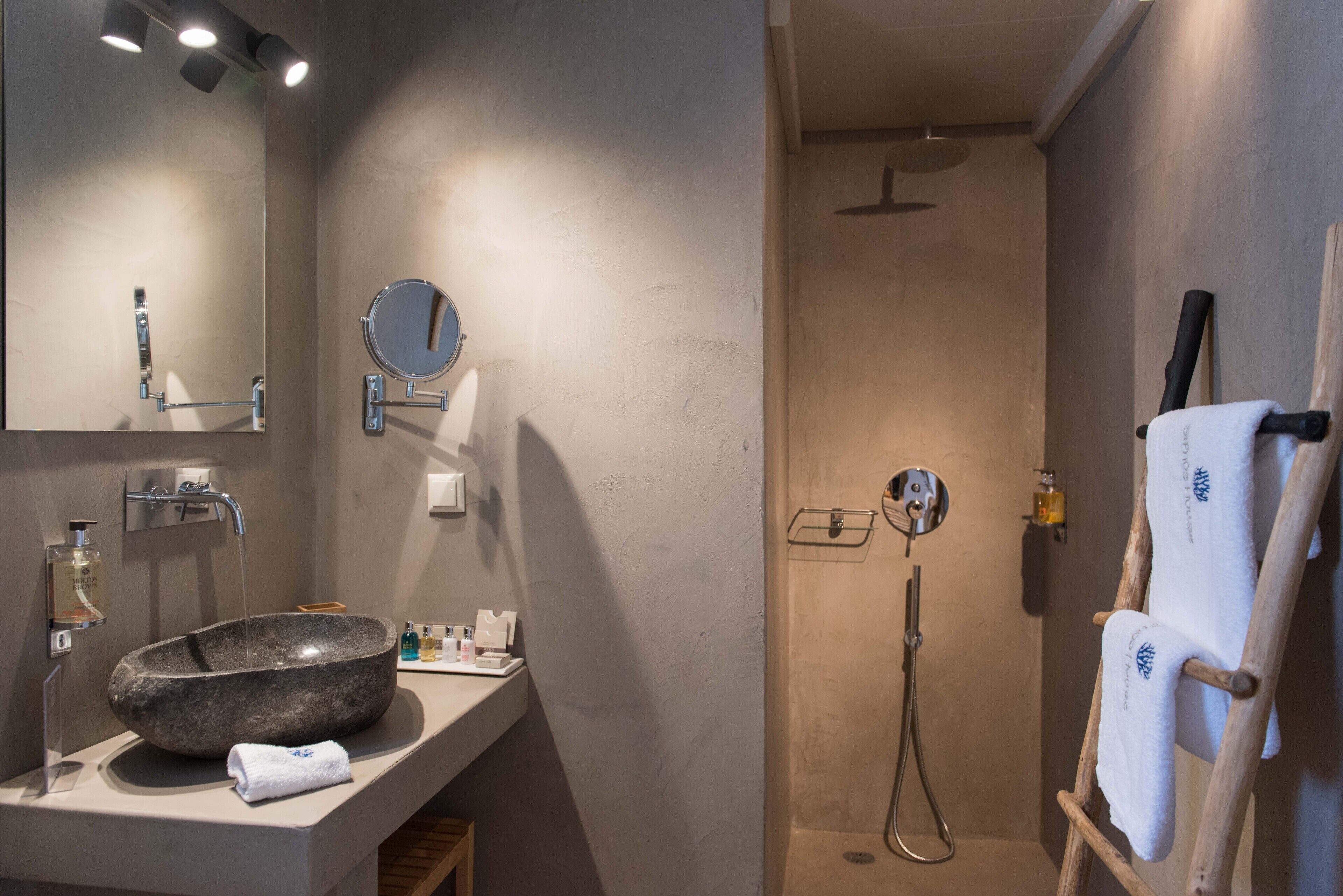 A modern bathroom with a large stone sink, a mirror, and a shower area.