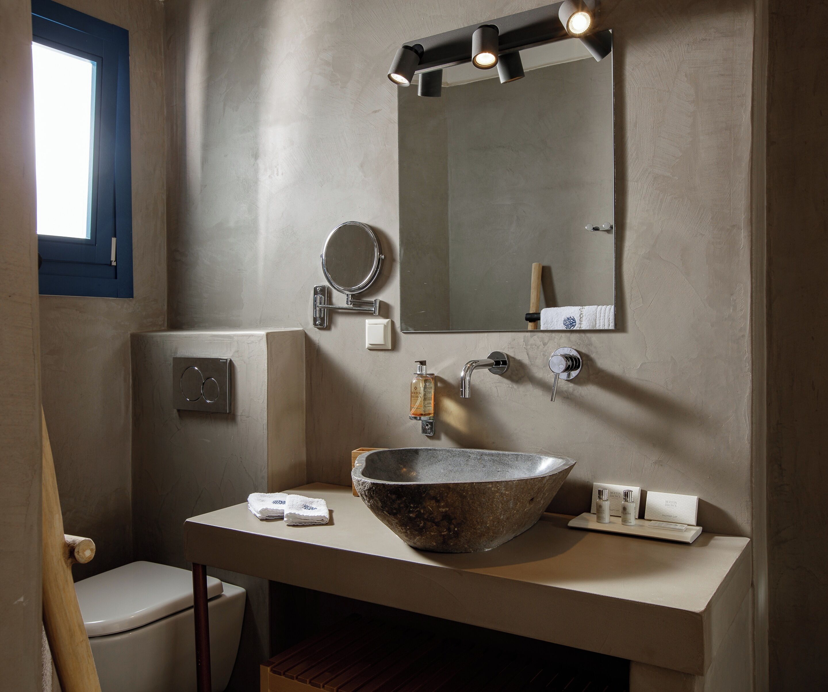 A bathroom with a large stone sink, a mirror, and a towel dispenser.